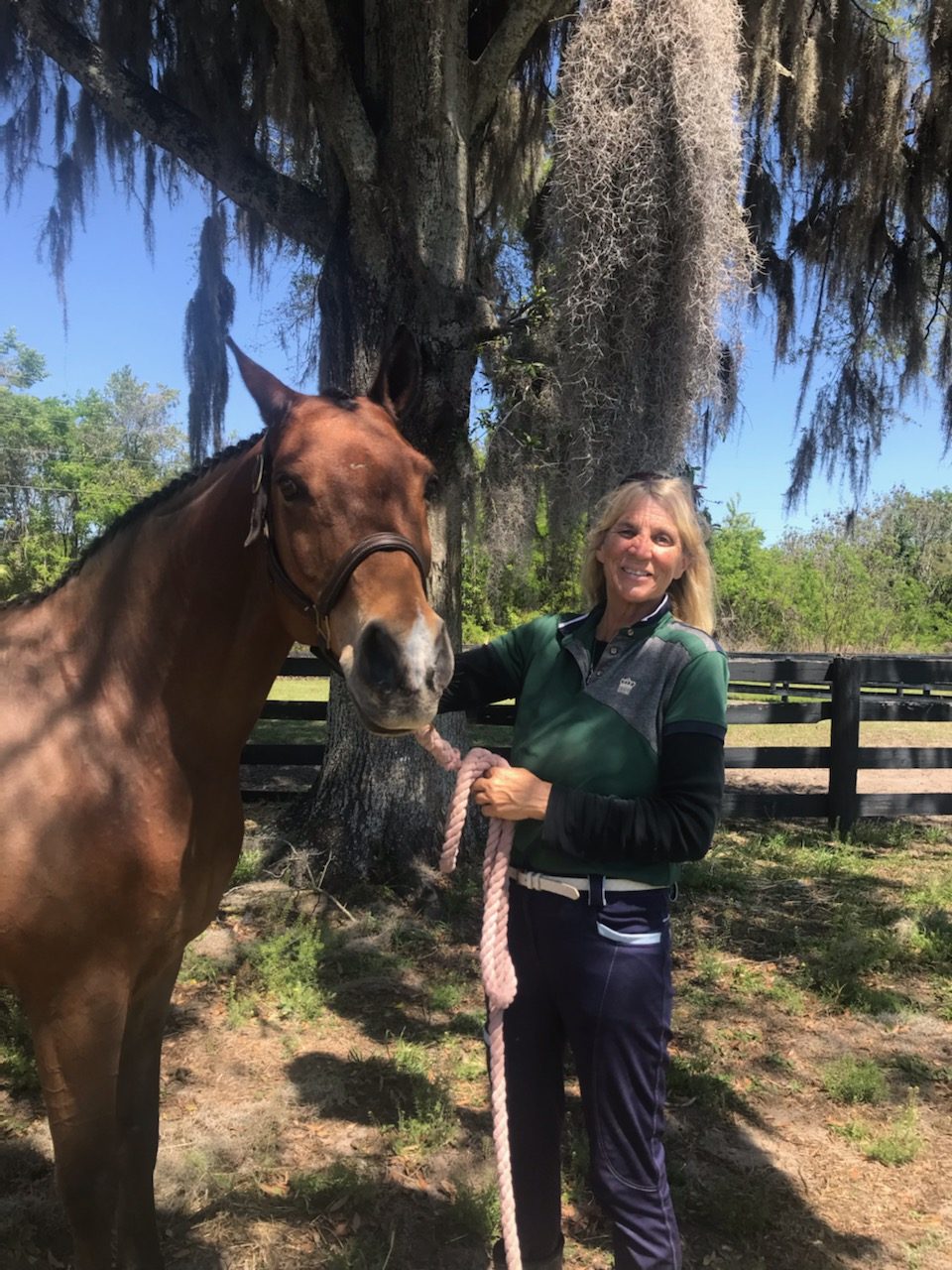 Kimber Sobeck smiling beside her bay horse under moss-draped oaks at a fenced Marion County farm
